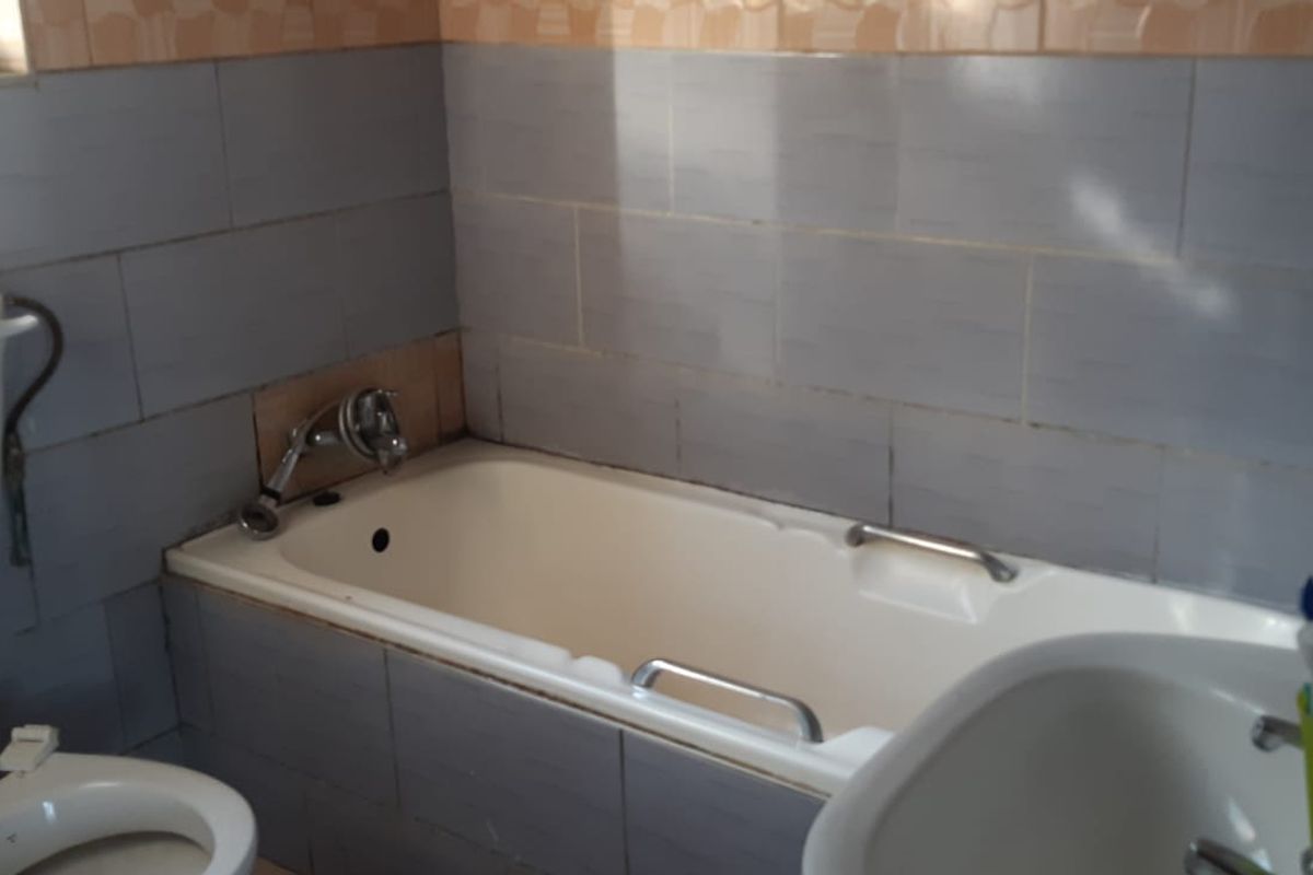 A functional bathroom featuring a standard bathtub, toilet, and washbasin with dated wall tiling throughout.