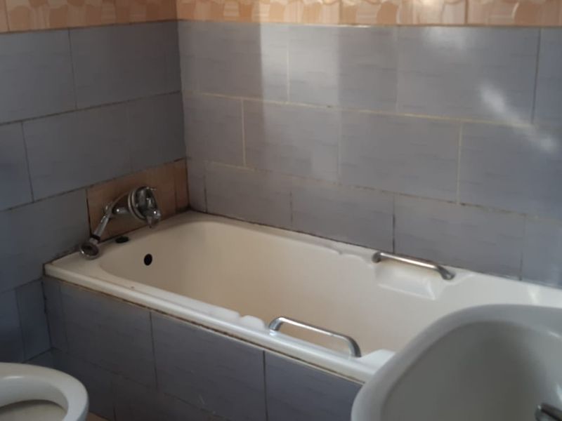 A functional bathroom featuring a standard bathtub, toilet, and washbasin with dated wall tiling throughout.