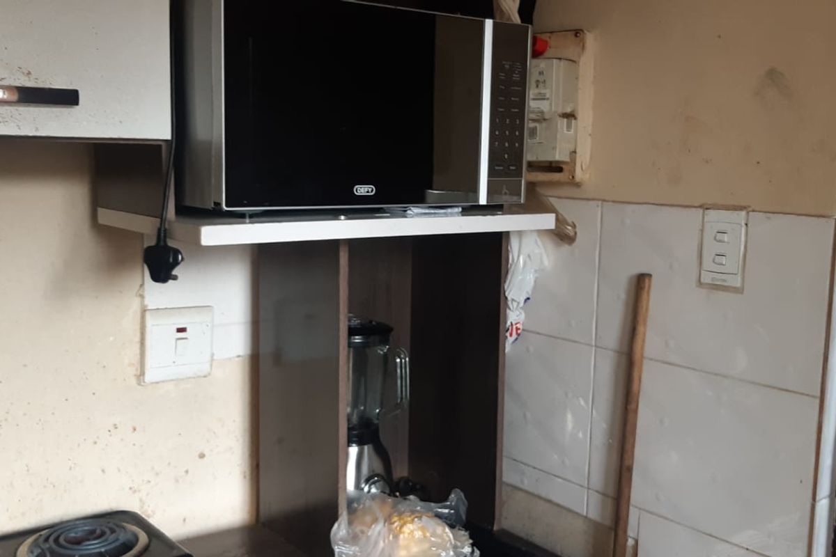 A compact kitchen area featuring built-in cabinetry and tiled splashbacks, currently showing significant wear and requiring cosmetic updates to improve the overall finish.