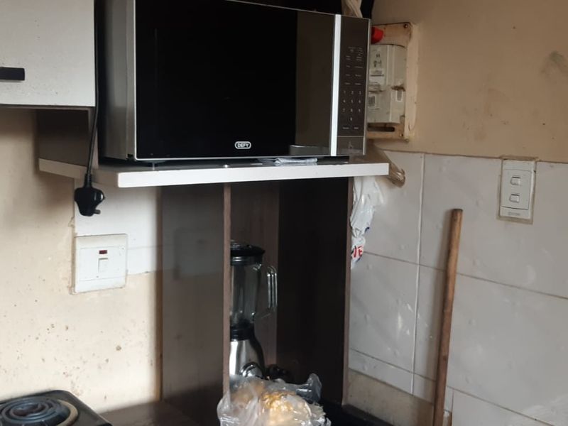 A compact kitchen area featuring built-in cabinetry and tiled splashbacks, currently showing significant wear and requiring cosmetic updates to improve the overall finish.