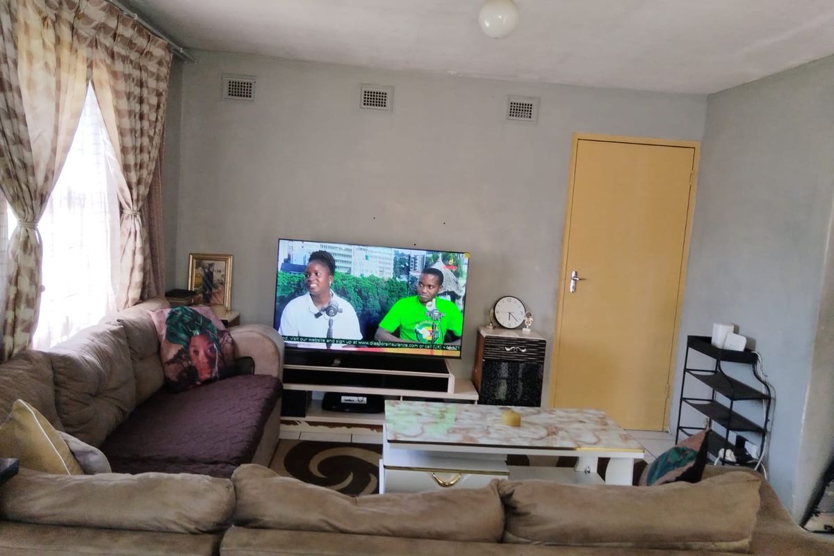 A living room featuring tiled flooring, wall-mounted air vents, and a standard internal door, showing signs of wear on the walls and ceiling.