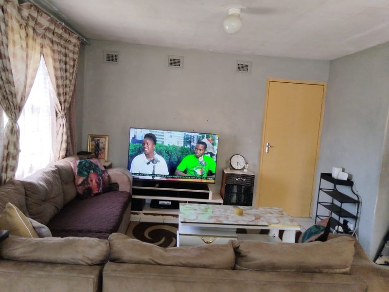 A living room featuring tiled flooring, wall-mounted air vents, and a standard internal door, showing signs of wear on the walls and ceiling.