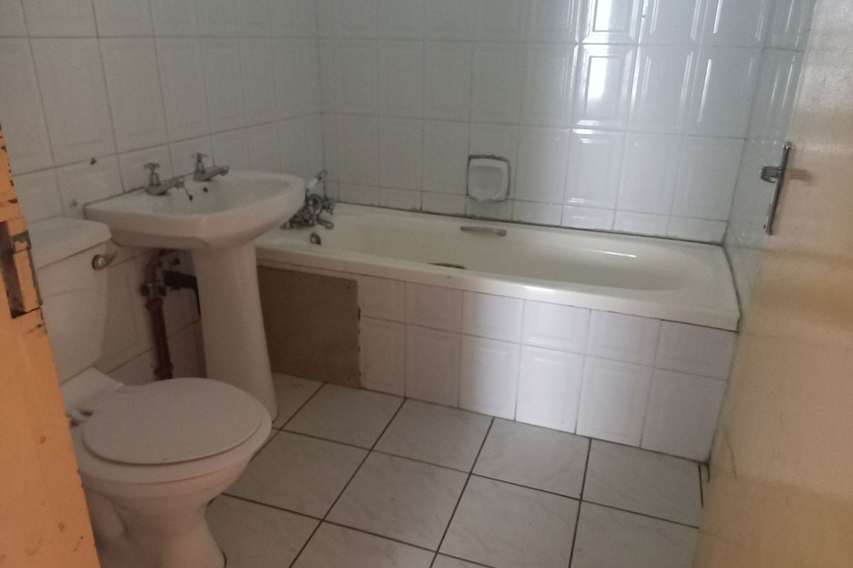 A functional bathroom featuring a pedestal basin, bathtub, and toilet with white ceramic wall and floor tiles, requiring some cosmetic updates to the paneling.