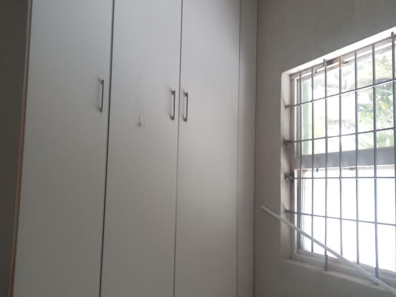A bedroom featuring a built-in wardrobe, security bars on the window, and a tiled ceiling. The space is vacant and requires minor cosmetic updates.