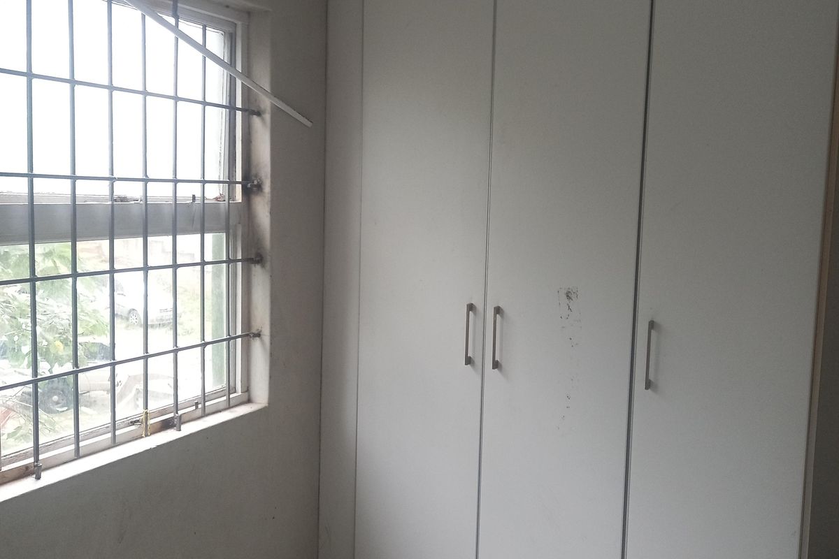 A vacant bedroom featuring tiled flooring, a built-in wardrobe, and a window fitted with security bars.