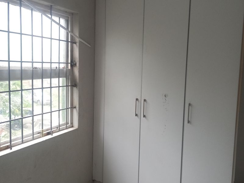 A vacant bedroom featuring tiled flooring, a built-in wardrobe, and a window fitted with security bars.