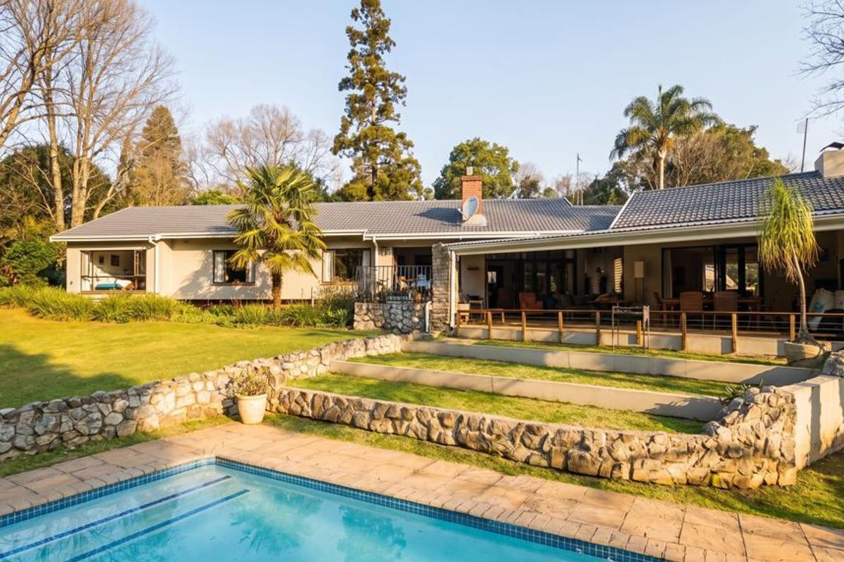 Spacious rear exterior view featuring a well-maintained swimming pool, stone retaining walls, a covered patio area, and a large landscaped garden.