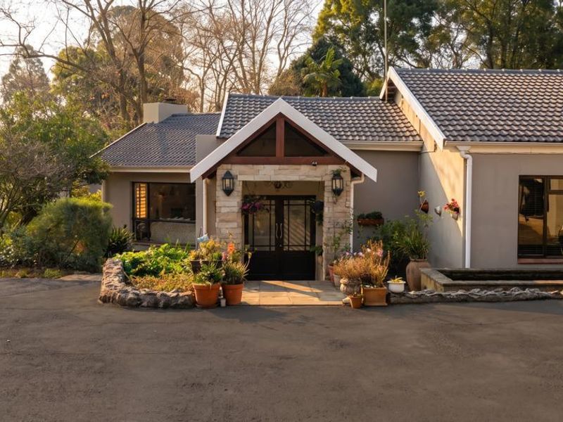 A well-maintained front facade featuring a tiled roof, stone-clad entrance gable, and a spacious asphalt driveway surrounded by mature trees.