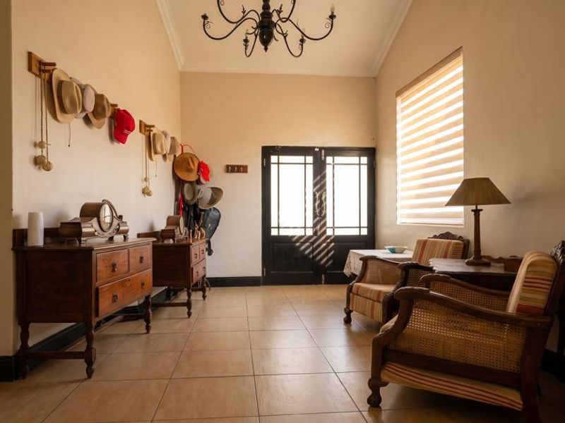A spacious entrance hall featuring tiled flooring, a decorative chandelier, and a double door entrance with natural light filtering through roller blinds.