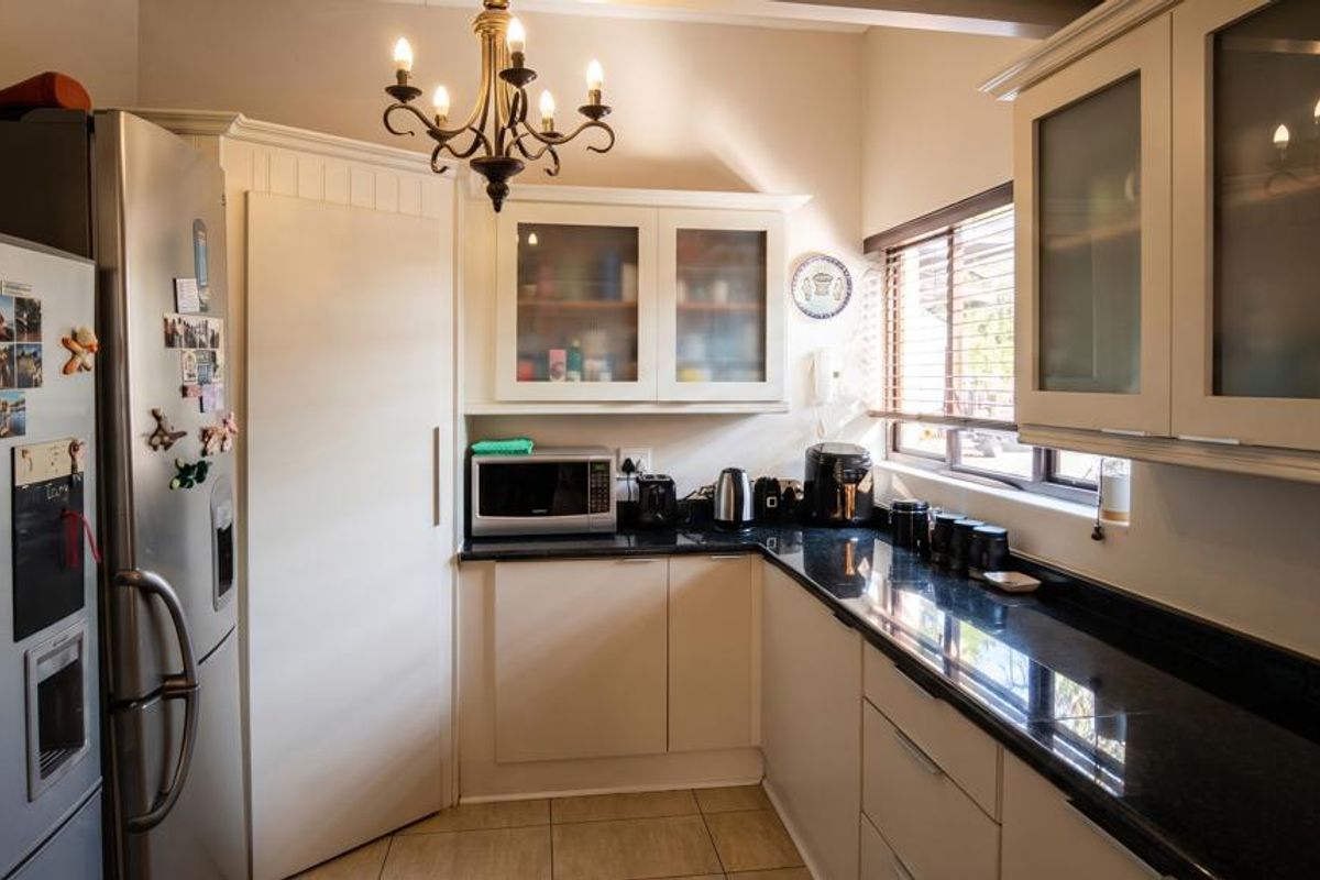 A well-maintained kitchen featuring granite countertops, ample built-in cabinetry with glass-fronted wall units, and tiled flooring.