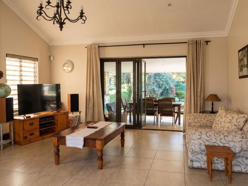 Spacious living room featuring vaulted ceilings, tiled flooring, a built-in fireplace, and large bi-fold doors opening to an outdoor patio area.