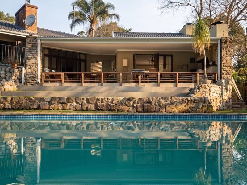 A well-maintained swimming pool area featuring a stone retaining wall, a spacious covered patio, and a tiled roof structure.
