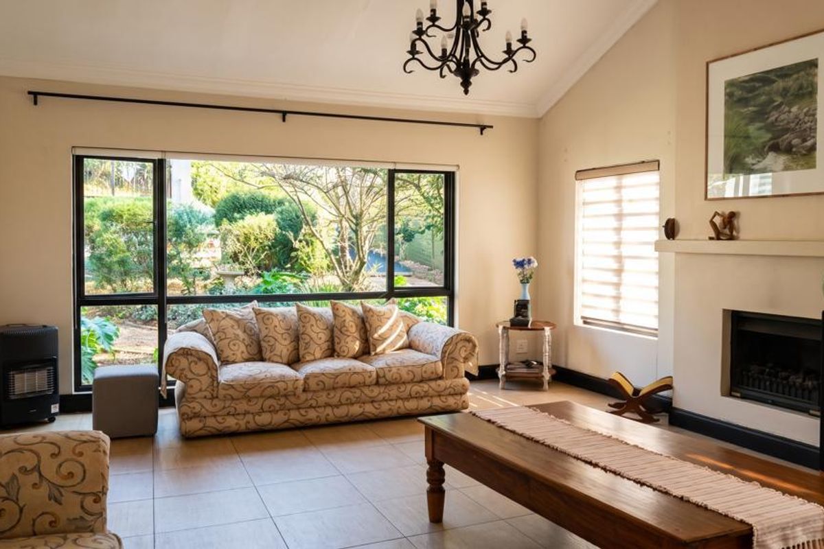 Spacious living room featuring a vaulted ceiling, tiled flooring, and a built-in fireplace, with large windows providing natural light and garden views.