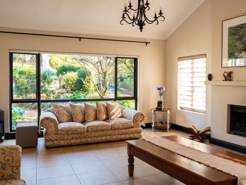 Spacious living room featuring a vaulted ceiling, tiled flooring, and a built-in fireplace, with large windows providing natural light and garden views.