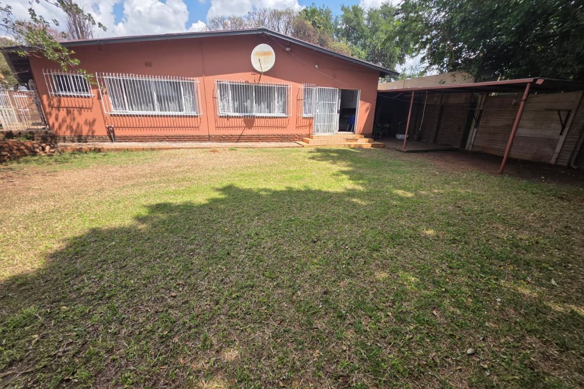 Rear view of the house featuring a spacious lawn, covered patio area, and exterior brick facade with security bars on windows.