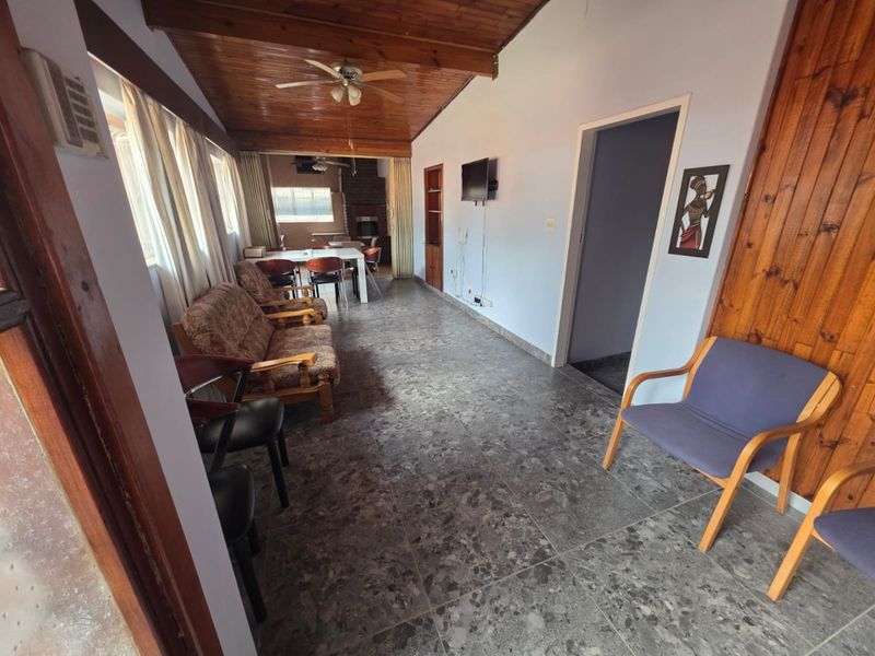 Open plan living and dining area featuring timber ceilings, tiled flooring, and a brick fireplace, offering a versatile space for relaxation and entertaining.