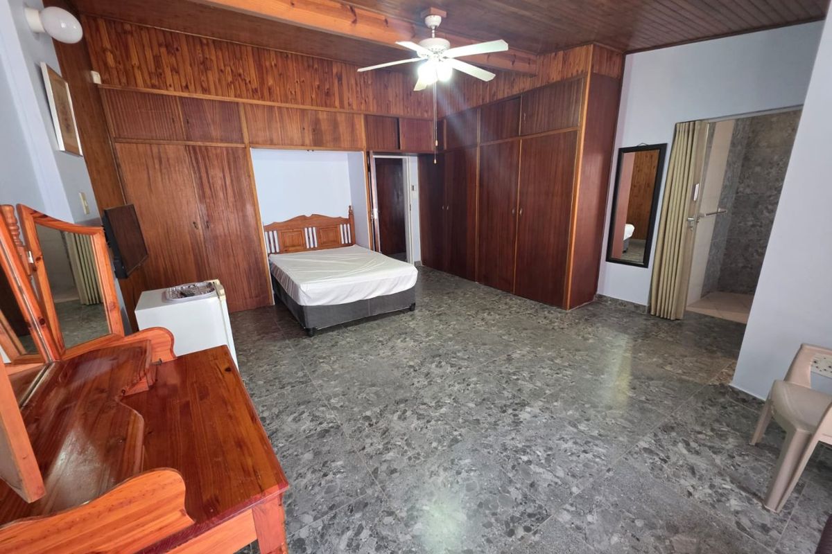Spacious bedroom featuring extensive built-in wooden cabinetry, a timber-clad ceiling with a central fan, and durable tiled flooring throughout.