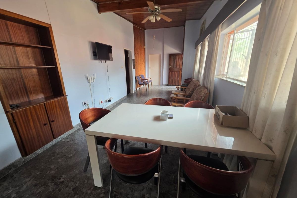A living area featuring a wooden ceiling with a fan, built-in shelving, and tiled flooring, offering a dated but functional space.