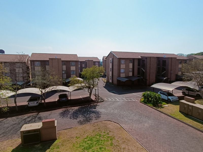 An aerial view of the apartment complex grounds, featuring paved driveways, covered parking bays, and well-maintained brick buildings with tiled roofs.