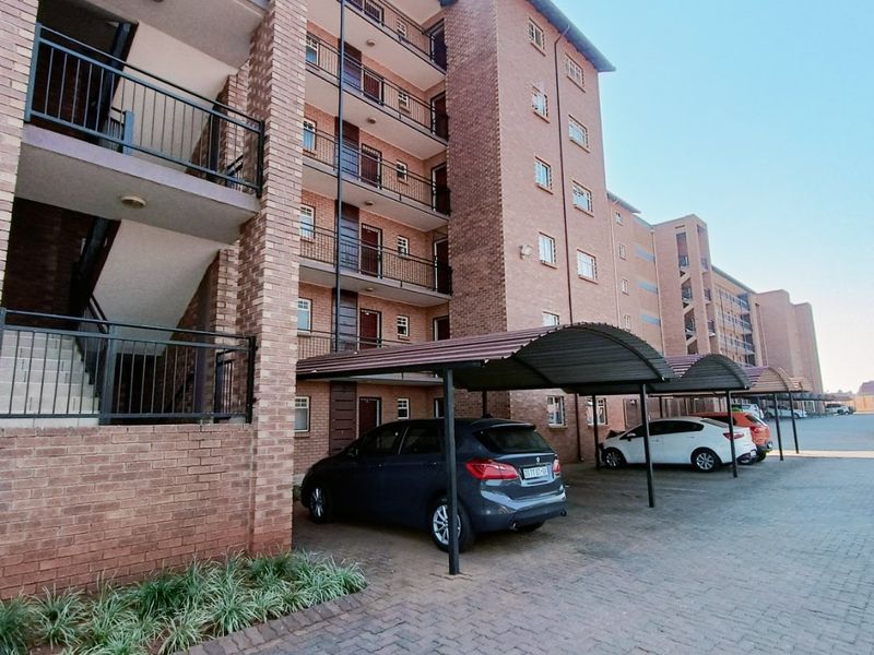 Exterior view of a multi-story brick apartment complex featuring covered parking bays, paved driveway, and external stairwell access to upper-level units.