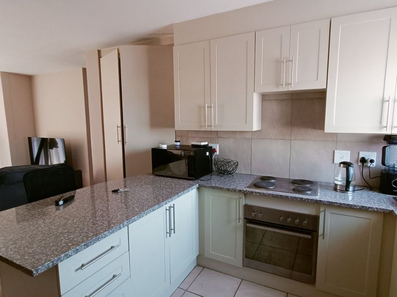 A functional kitchen featuring granite countertops, built-in cabinetry, an integrated oven, and an electric hob, seamlessly connected to the living area.