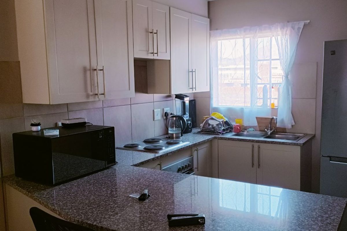 A functional kitchen featuring granite countertops, ample built-in cabinetry, an electric hob, and a stainless steel sink with a tiled backsplash.
