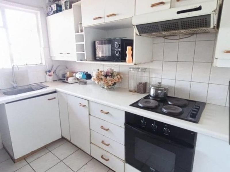 A functional kitchen featuring white cabinetry, tiled backsplash, built-in oven with electric hob, and tiled flooring, offering a clean but dated aesthetic.