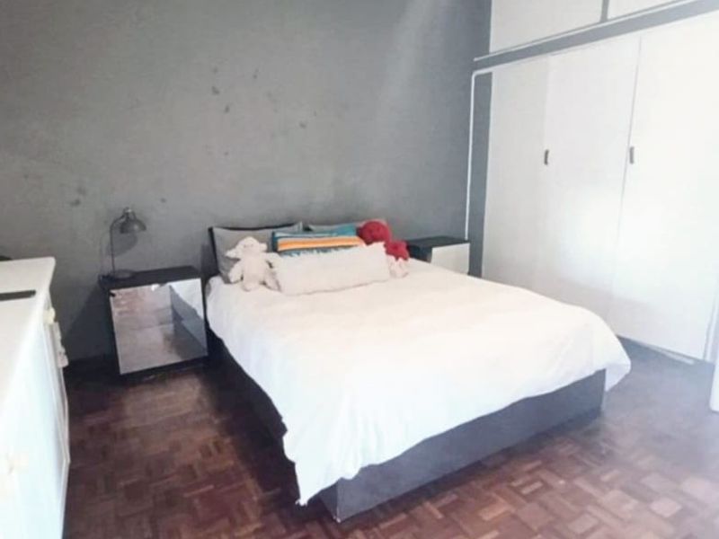 A bedroom featuring parquet flooring, built-in cupboards with overhead storage, and a grey feature wall.