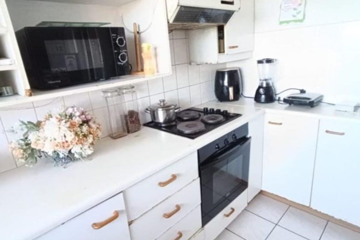 A functional kitchen featuring white cabinetry, a built-in oven, electric hob, extractor fan, and tiled flooring with a classic backsplash.