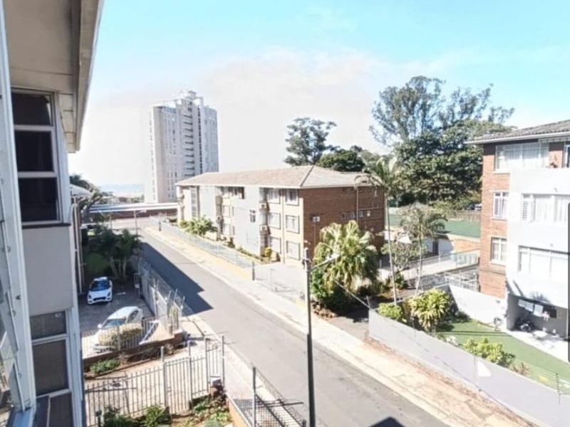 Elevated view overlooking the surrounding residential street, neighbouring apartment buildings, and distant coastal horizon.