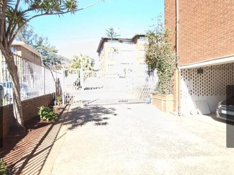 Exterior view of the apartment complex entrance featuring a concrete driveway, secure metal gate, and covered parking area.