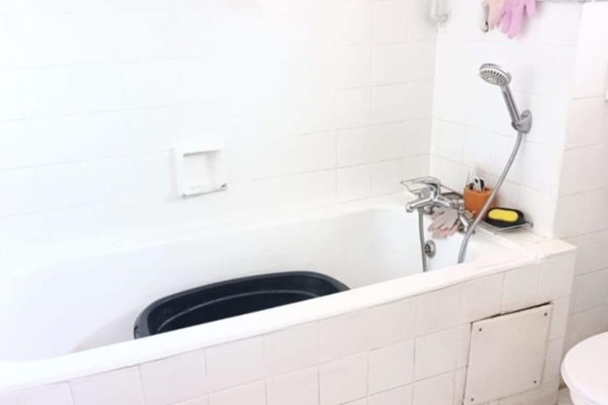 A dated bathroom featuring a built-in bathtub with a handheld shower attachment, white wall tiles, and floor tiles, requiring cosmetic updates.