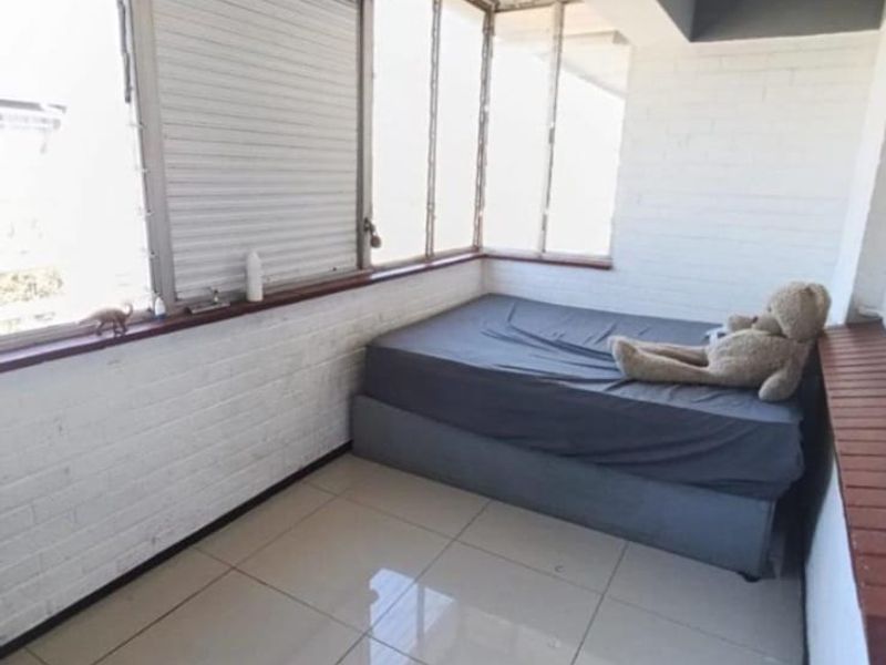 A compact bedroom featuring tiled flooring, painted brick walls, and large windows with an integrated roller shutter for privacy.