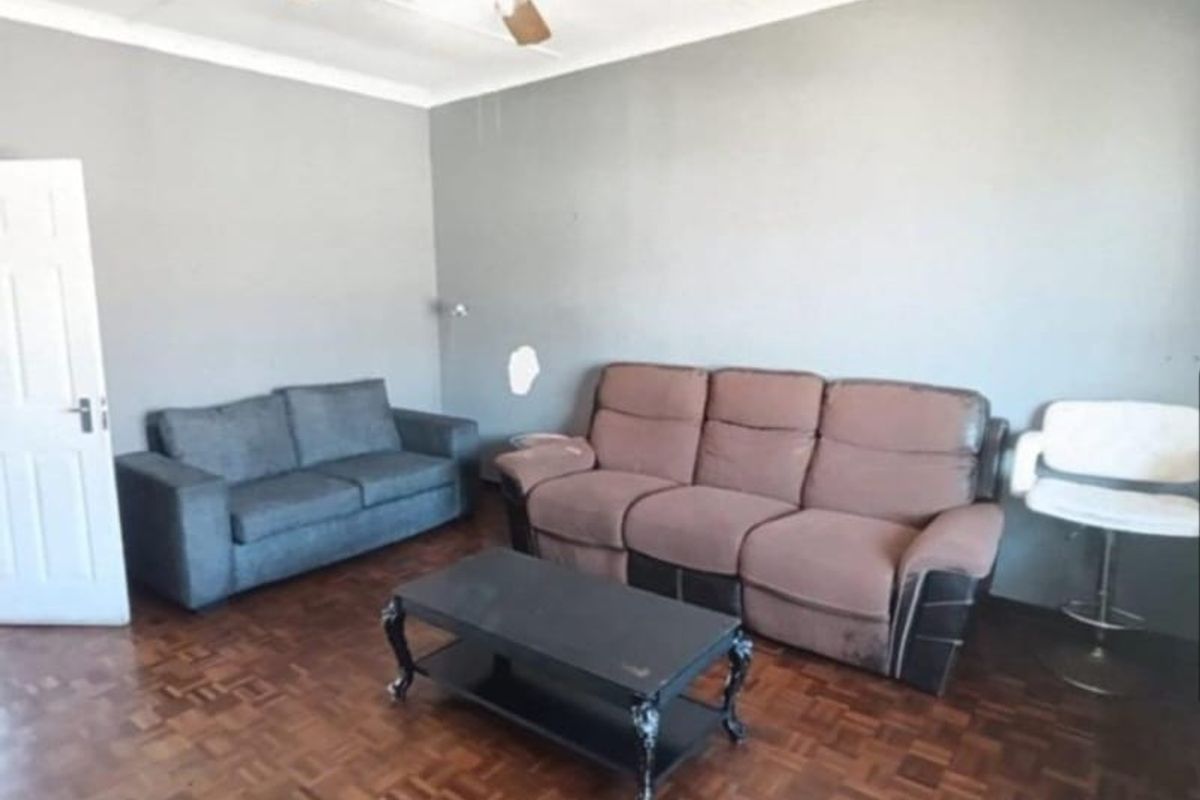 A living room featuring parquet flooring, a ceiling fan, and coved ceilings, with visible wall surface damage requiring repair.