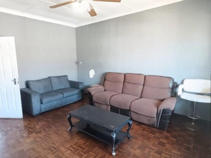 A living room featuring parquet flooring, a ceiling fan, and coved ceilings, with visible wall surface damage requiring repair.