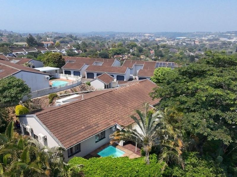 Aerial view of a townhouse complex featuring tiled roofs, private swimming pools, and established surrounding greenery with expansive suburban views.