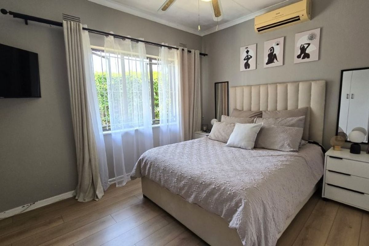 A well-maintained bedroom featuring laminate flooring, a ceiling fan, and a wall-mounted air conditioning unit, offering a comfortable and functional living space.
