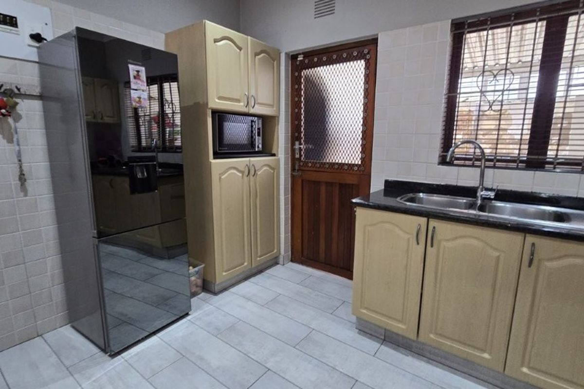 A functional kitchen featuring light-toned cabinetry, granite countertops, a double sink, and tiled finishes, providing a practical workspace with direct exterior access.
