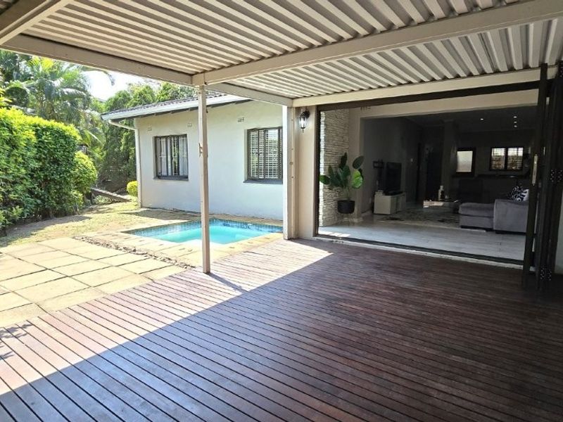 Spacious covered patio featuring timber decking, seamlessly connecting to the interior living area through folding glass doors, overlooking a private swimming pool.