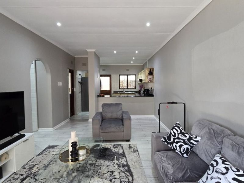 An open-plan living area featuring tiled flooring, recessed lighting, and a seamless transition into the kitchen space with built-in cabinetry.