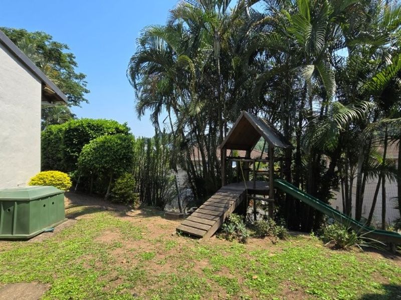 A private garden area featuring mature palm trees, established shrubs, and an exterior wall-mounted air conditioning unit.