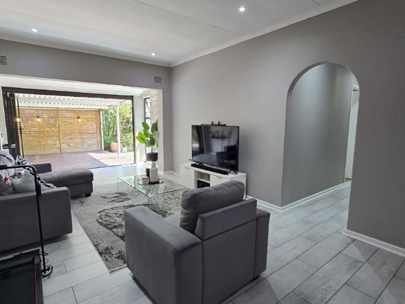 Spacious living room featuring modern tiled flooring, recessed downlights, and an elegant archway leading to a seamless transition to the outdoor patio area.