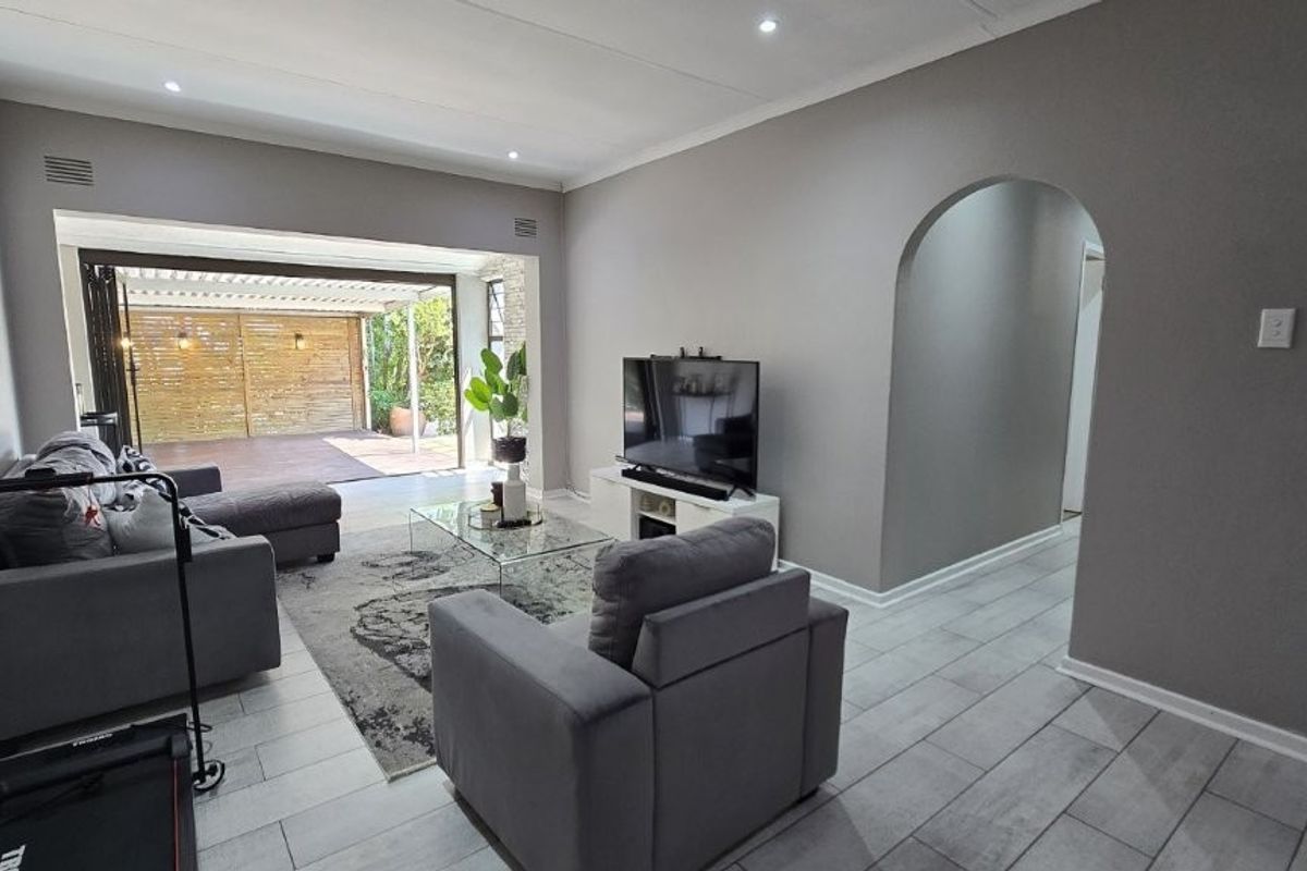 Spacious living room featuring modern tiled flooring, recessed downlights, and an elegant archway leading to a seamless transition to the outdoor patio area.