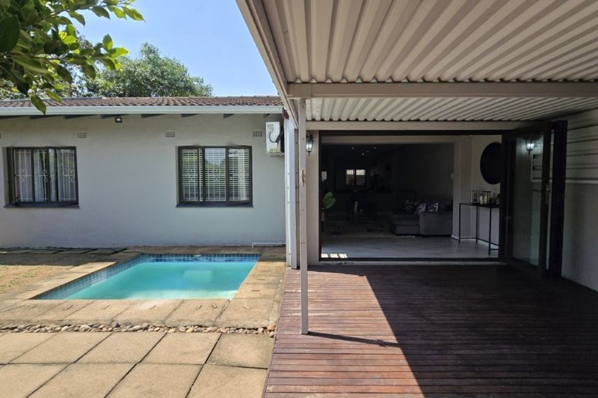 Rear exterior view featuring a covered timber deck, swimming pool, and direct access to the interior living space through large sliding doors.