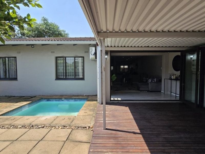 Rear exterior view featuring a covered timber deck, swimming pool, and direct access to the interior living space through large sliding doors.