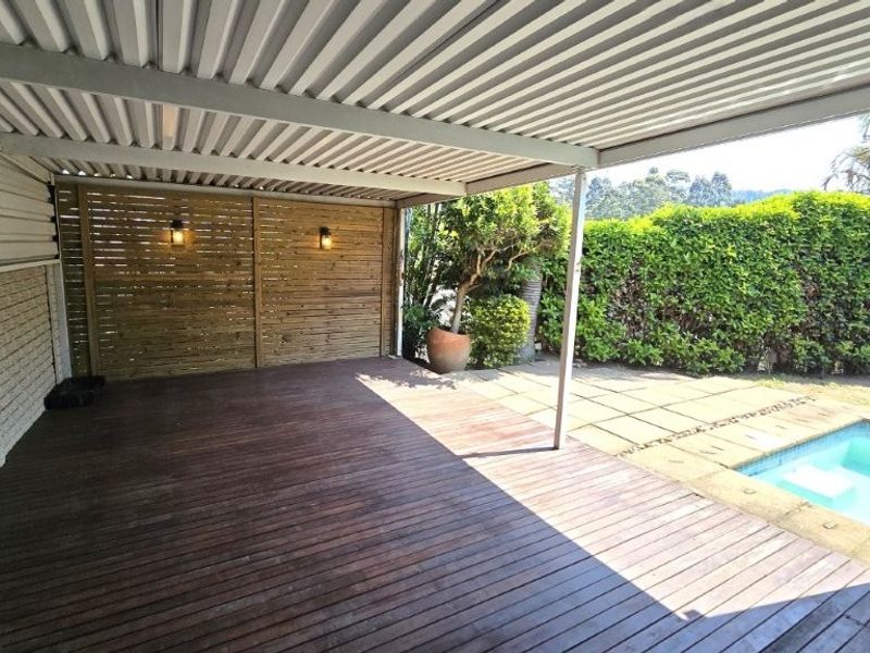 Covered outdoor patio featuring timber decking, a privacy screen, and direct access to a private swimming pool area.