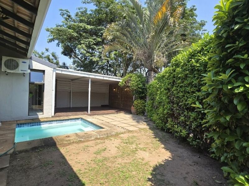 Rear exterior view featuring a small swimming pool, a covered patio area, and established garden hedging.