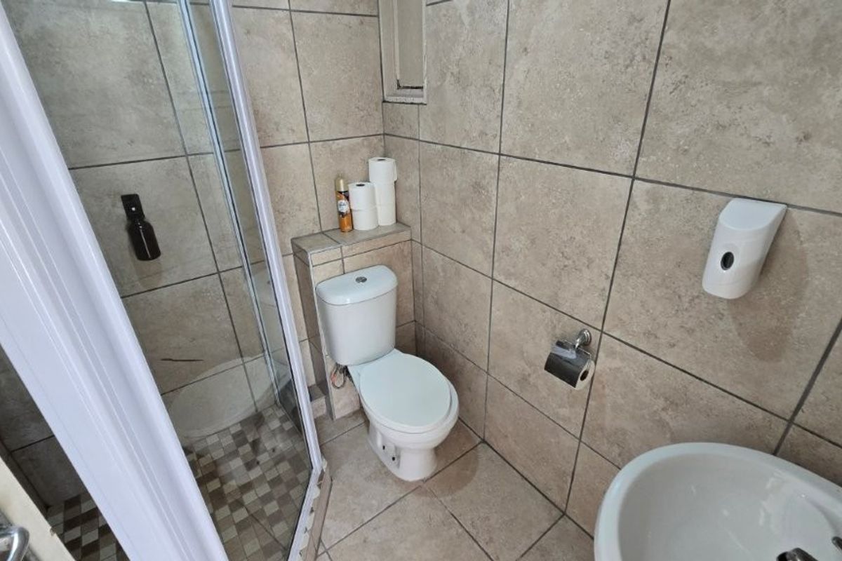 A functional bathroom featuring a shower enclosure, toilet, and washbasin with neutral wall and floor tiling.