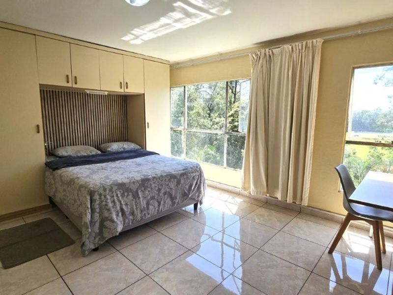 A spacious bedroom featuring extensive built-in cupboards, tiled flooring, and large windows providing natural light and garden views.