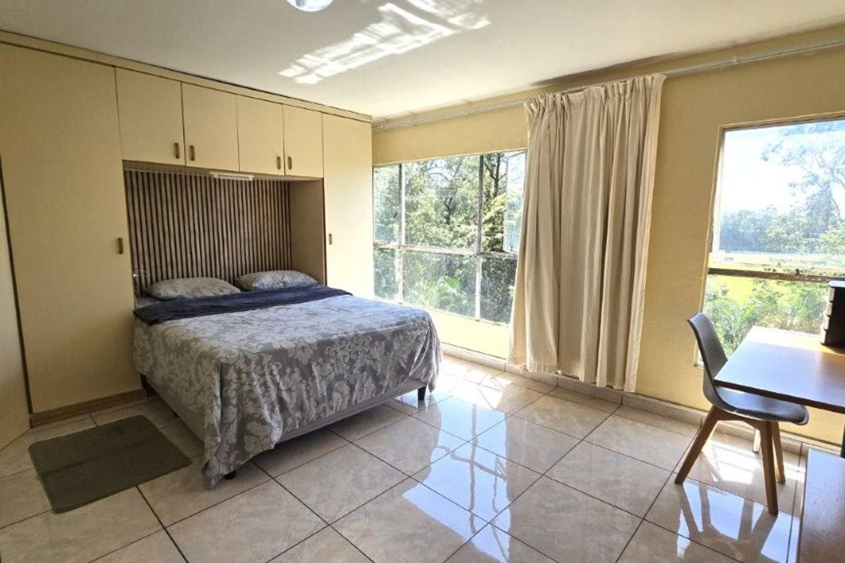A spacious bedroom featuring extensive built-in cupboards, tiled flooring, and large windows providing natural light and garden views.